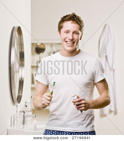 Man in pajamas in bathroom holding toothbrush and toothpaste
