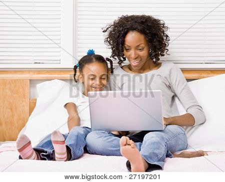 Madre e figlia digitando sul computer portatile sul letto in camera da letto