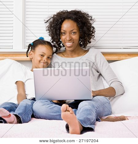 Madre e figlia digitando sul computer portatile sul letto in camera da letto