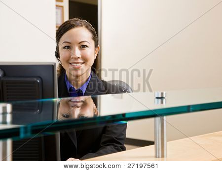 Smiling receptionist with telephone earpiece working at desk in office