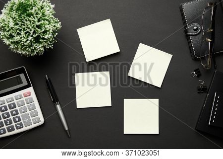 Top view of modern black office desk with calc, notebook, pen, blank sticker and a lot of things. Flat lay table layout. Copy space for text.
