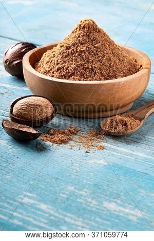 Whole Inshell Nut, Cracked And Nutmeg Powder In A Wooden Bowl And Spoon On Old Blue Rustic Backgroun