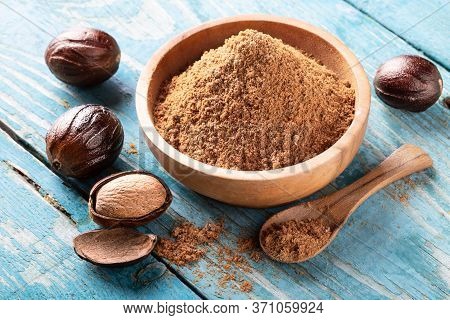 Whole Inshell Nut, Cracked And Nutmeg Powder In A Wooden Bowl And Spoon On Old Blue Rustic Backgroun