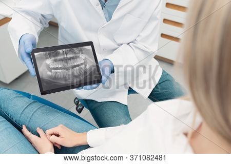 Dental Consultation In Clinic. Dentist Showing Teeth X-ray On Digital Tablet Screen
