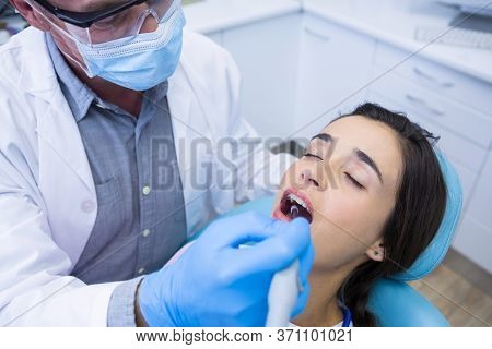 High angle view of dentist holding tools while treating woman at medical clinic