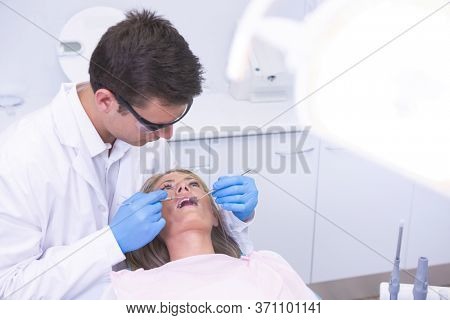 High angle view of dentist holding equipment while examining woman at medical clinic