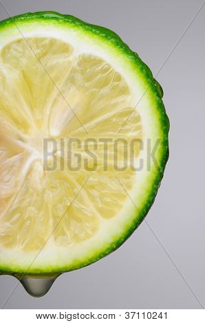 Makro skud af en lime skive over en grå baggrund. Lodret format med et drop af juice på botto
