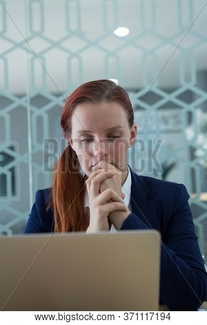Thoughtful businesswoman using laptop at desk in office