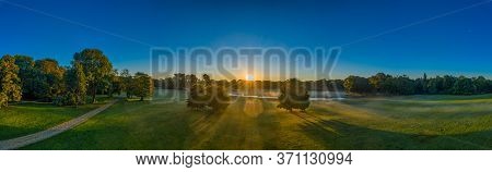 Wonderful Panorama Of The English Garden In Munich, Bavaria, Germany. Early Fog Is Rising While The 
