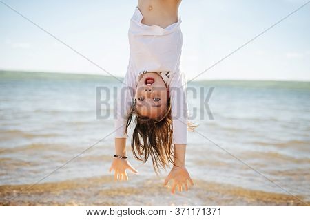 Little Hiperemotional School Age Girl Hanging Upside Down. On A Lake Shoreside.