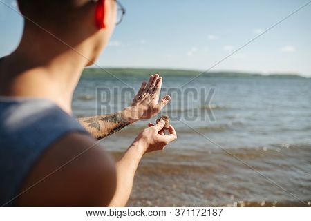Adult Man Aiming With His Hand, Throwing Pebbels Against Lake Water On Sunny Day