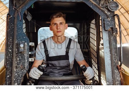 A Man In Overalls Driving A Tractor. Worker Sitting On His Tractor