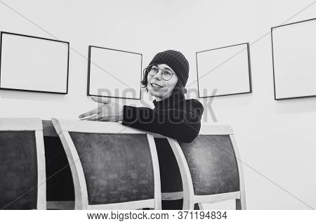 A Girl With Glasses Talks And Gestures Against A Background Of Empty Pictures. Artist At The Present