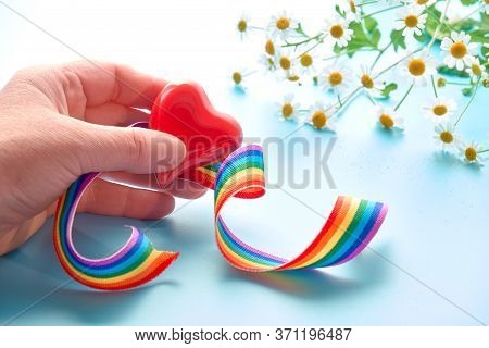 Red Heart And Curled Rainbow Ribbon In Adult Female Hand. Camomile Flowers On Light Blue Mint Backgr