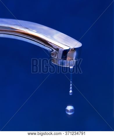 Drops Of Water Dripping From The Iron Crane On Blue Background. Concept Of Rational Use Of Natural R