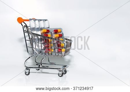 Miniature Shopping Cart Filled With Tablets And Capsules On A White Background, Medicine And Coronav