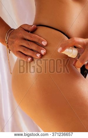 Suntan Lotion In Spray Bottle. Young Woman In Spraying Tanning Oil On Her Leg From Bottle.