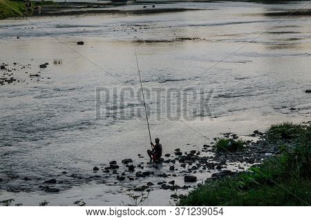 Silhouettes Of The Fisherman. Fisherman Fishing On A Fishing Rod In The River In The Evening