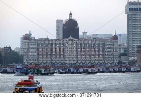 MUMBAI, INDIA - FEBRUARY 15, 2020: Taj Mahal hotel, Gateway of India and tourist boats in water of Arabian Sea in Mumbai, India