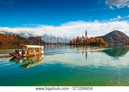 Church Of Assumption In Lake Bled, Slovenia With Blue Sky, Touristic Boat And Clouds In The Autumn