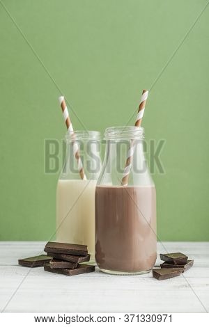Two Bottles Chocolate And Vanila Milk With Drinking Straws On Green Background
