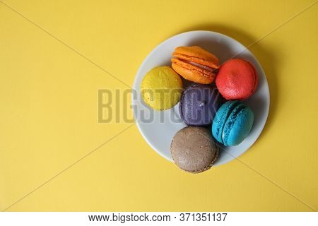 Macaroons Of Differrent Colours On A Saucer Isolated On Yellow Background Flat Lay. Image Contains C