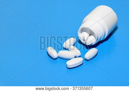 White Tablets Scattered From A Plastic Bottle On A Blue Background. Top View With Copy Space.