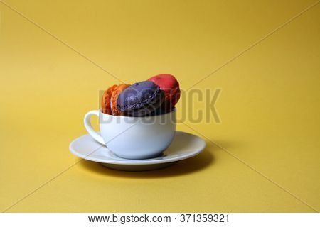 Macaroons Of Differrent Colours In A Tea Cup Isolated On Yellow Background. Image Contains Copy Spac
