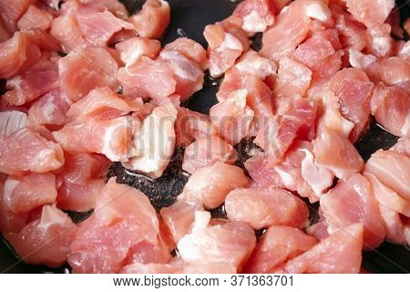 Raw Sliced Small Pieces Of Pork Meat Are Fried In A Pan In Olive Oil. Close Up Selective Focus