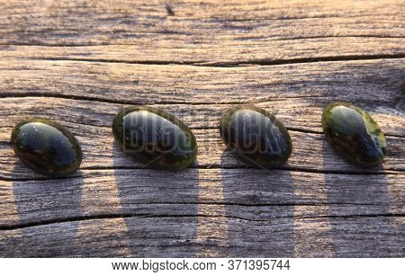 Black Jade Translucent Green Stone In Sunlight On Wood. The Black Jade Is Dark Green In Color, But U