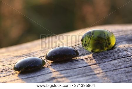 Black Jade Translucent Green Stone In Sunlight On Wood. The Black Jade Is Dark Green In Color, But U