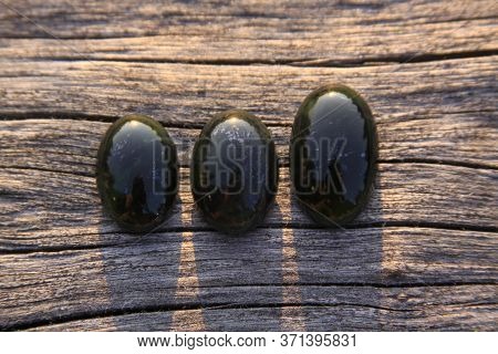 Black Jade Translucent Green Stone In Sunlight On Wood. The Black Jade Is Dark Green In Color, But U