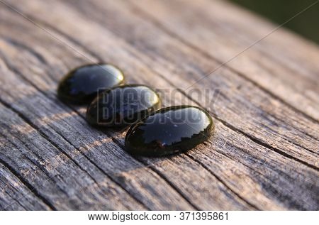 Black Jade Translucent Green Stone In Sunlight On Wood. The Black Jade Is Dark Green In Color, But U
