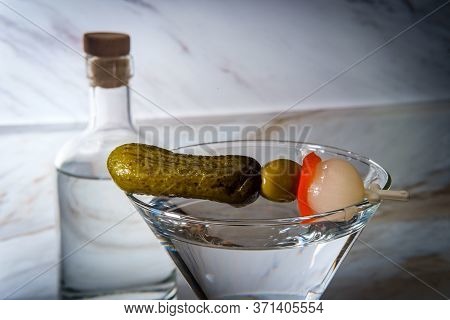 Dry Gin Martini Served Neat With Pickle Cocktail Stirrer And Bottle In Background
