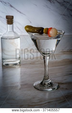 Dry Gin Martini Served Neat With Pickle Cocktail Stirrer And Bottle In Background