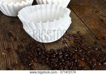 An Image Of Several White Basket Style Coffee Filers And Dark Roasted Coffee Beans.