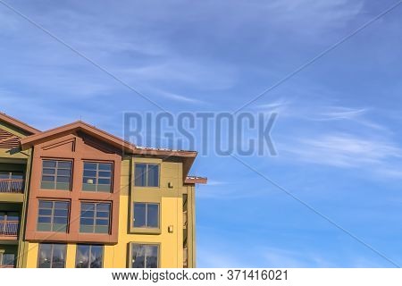 Home Exterior With Balconies And Multi Color Walls Against Blue Sky And Clouds