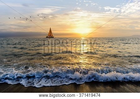 A Sailboat Is Sailing Along The Ocean As Birds Fly In The Sunset Sky
