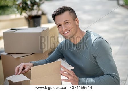 Smiling Handsome Man Sitting Next To The Cardboards
