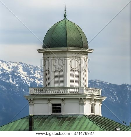 Square Building Exterior With Green Dome And Roof Against Snowy Mountain And Cloudy Sky