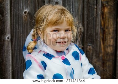 Outdoor Portrait Of Happy Smiling Little Toddler Girl Wearing Rain Jacket On Rainy Cloudy Day. Cute 
