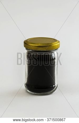 Small Glass Jar Of Dark Honey With Metallic Cap Isolated On A White Background.
