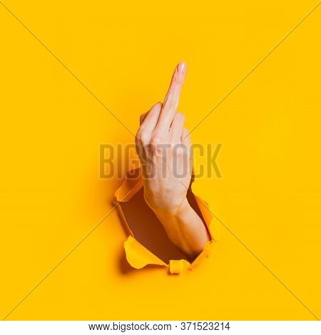 Female Hand Showing Gesture Meaning Fuck You Or Fuck Off Through The Hole In The Yellow Paper Backgr