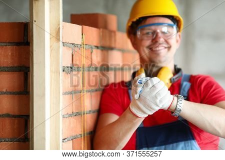 Builder In Helmet Stands Near Brickwork And Smiles. Appearance Brick Walls Is Presentable. Brick Spe