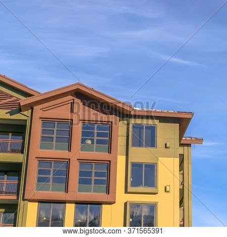 Square Home Exterior With Balconies And Multi Color Walls Against Blue Sky And Clouds
