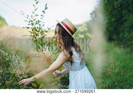 Beautiful Girl In A Board And Hat Collects Flowers. The Girl Collects A Bouquet Of Dried Flowers. Br