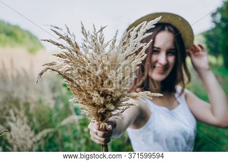 Happy Young Woman In A White Dress In A Straw Hat. Smiling Girl With A Bouquet Of Dried Flowers. Gir