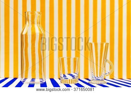 Transparent Glassware-glasses And A Bottle On A Striped Background. White And Yellow Striped Backgro