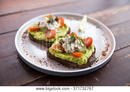 Smashed Avocado Toasts With Cherry Tomatoes And Crumbled Feta Cheese On A Plate On Rye Bread. Health