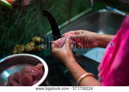 An Indian Woman Cutting Pieces Of Chicken With Boti, A Long Curved Knife Fixed On A Wooden Platform